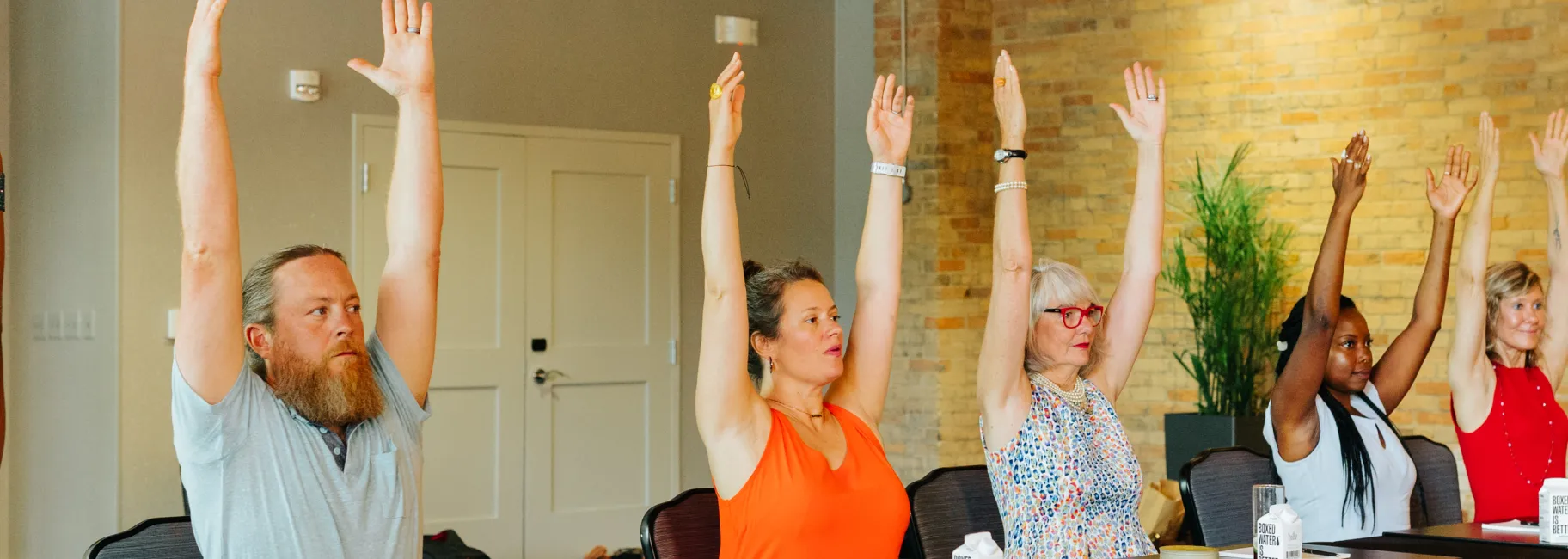Group of adults sitting at conference table doing yoga stretch break