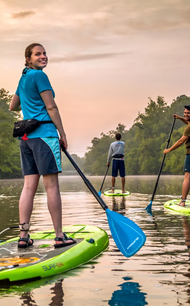 Three people paddle down an Asheville waterway at sunset