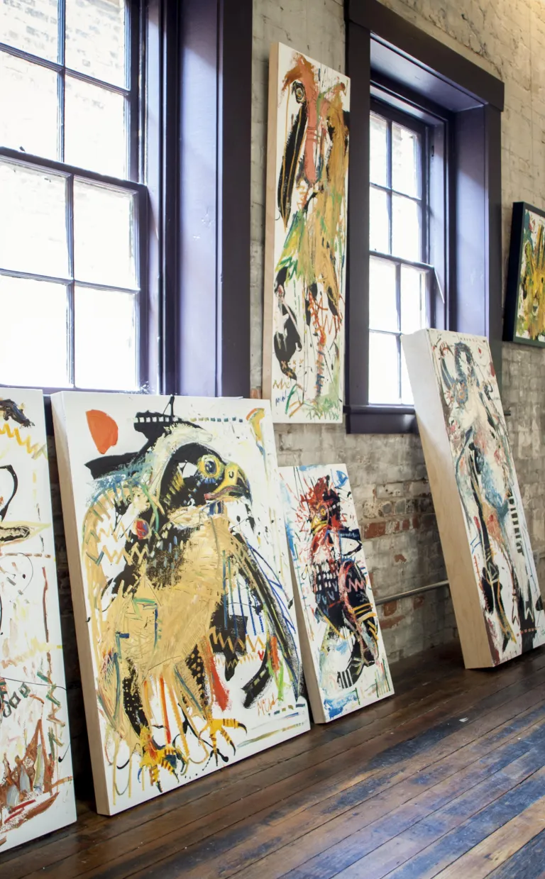 An artists kneels beside several large painting canvases in Asheville