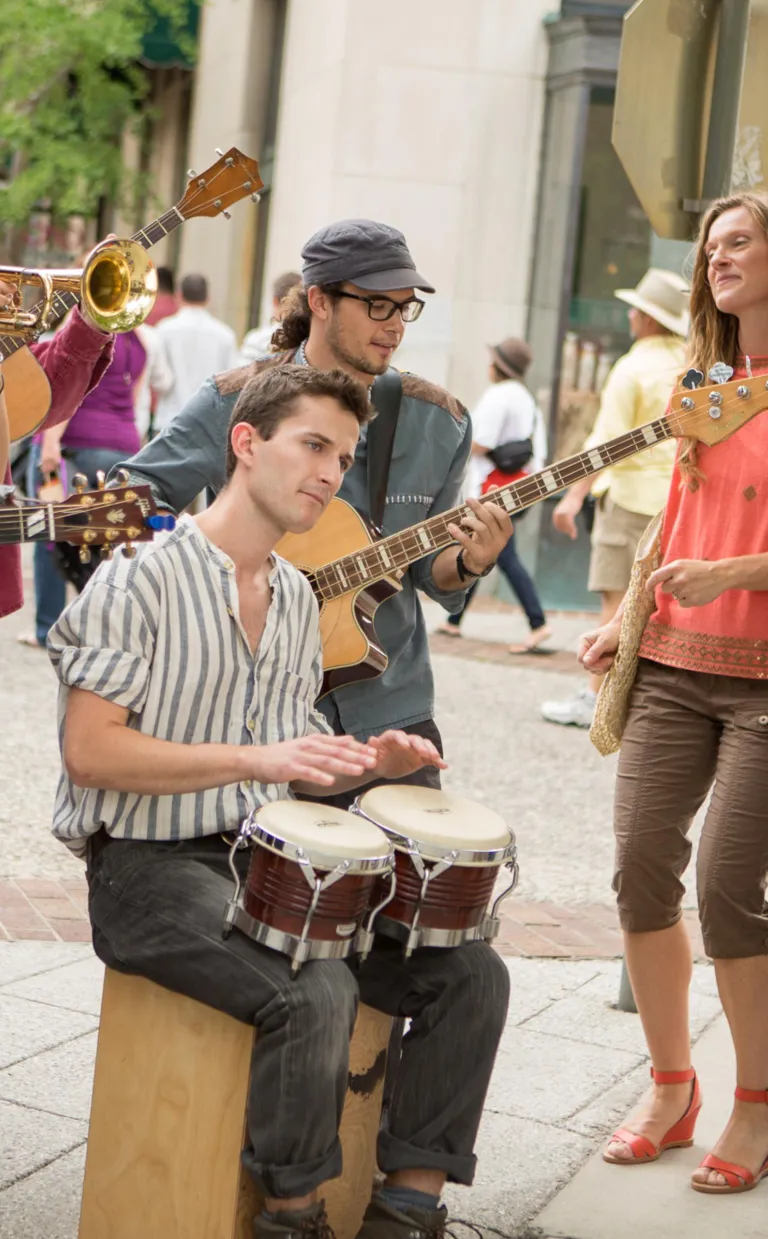 A busker sits amid other musicians and an audience playing the bongos in Asheville