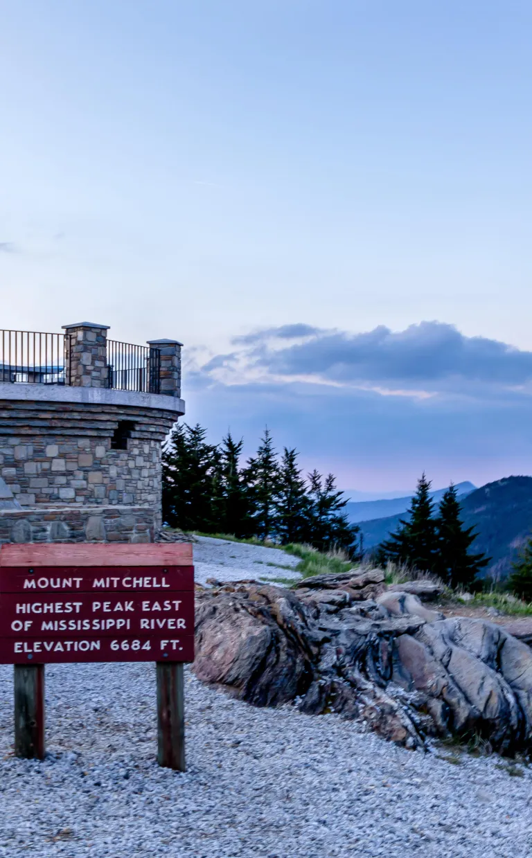 a sign read "Mt. Mitchell" at sunset, overlooking beautiful mountains