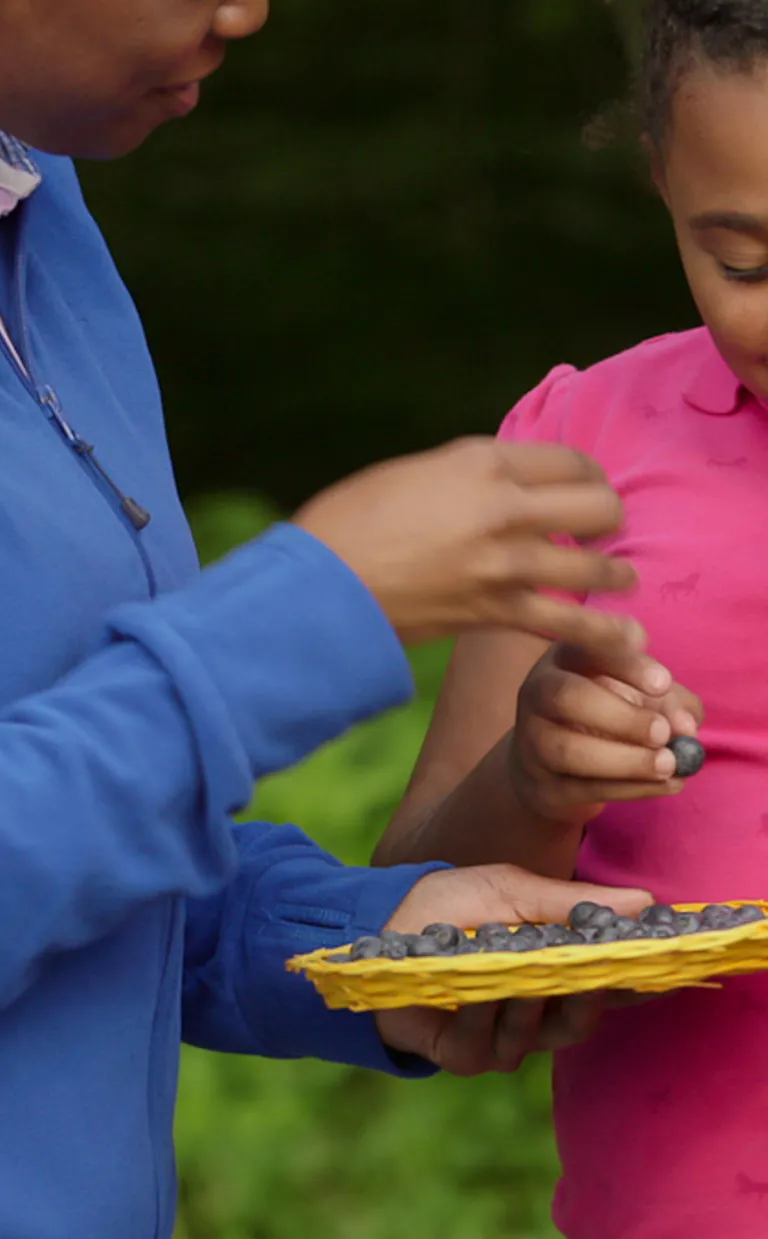 A parent and child smile as they eat fresh-picked berries in Asheville