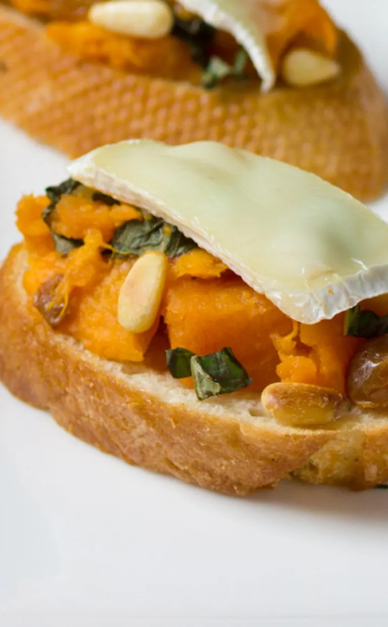 bruschetta with diced sweet potato and cheese sit on a white plate