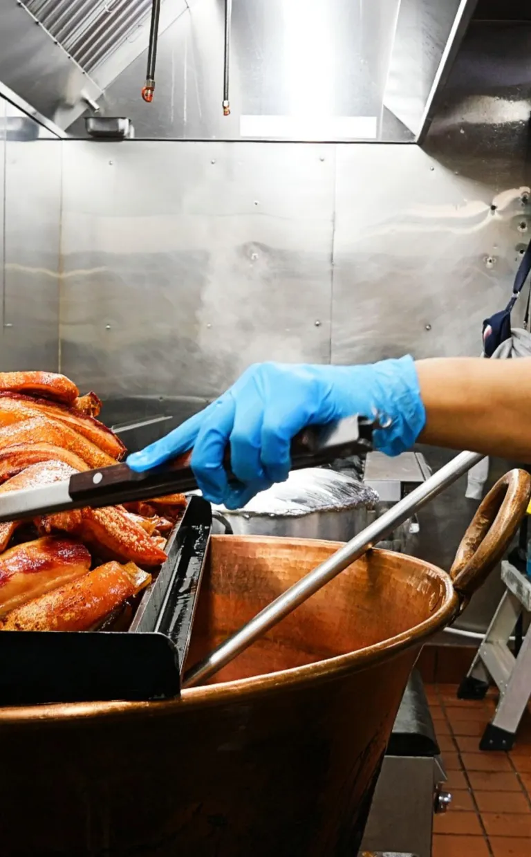 A chef cooks pork over a large copper vat