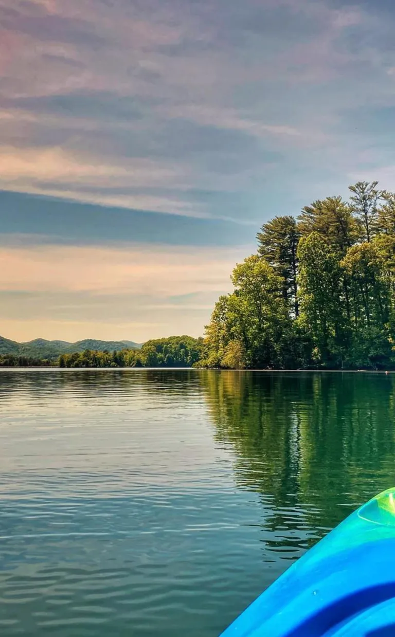 a kayak floats on a lake looking at a shore at sunset